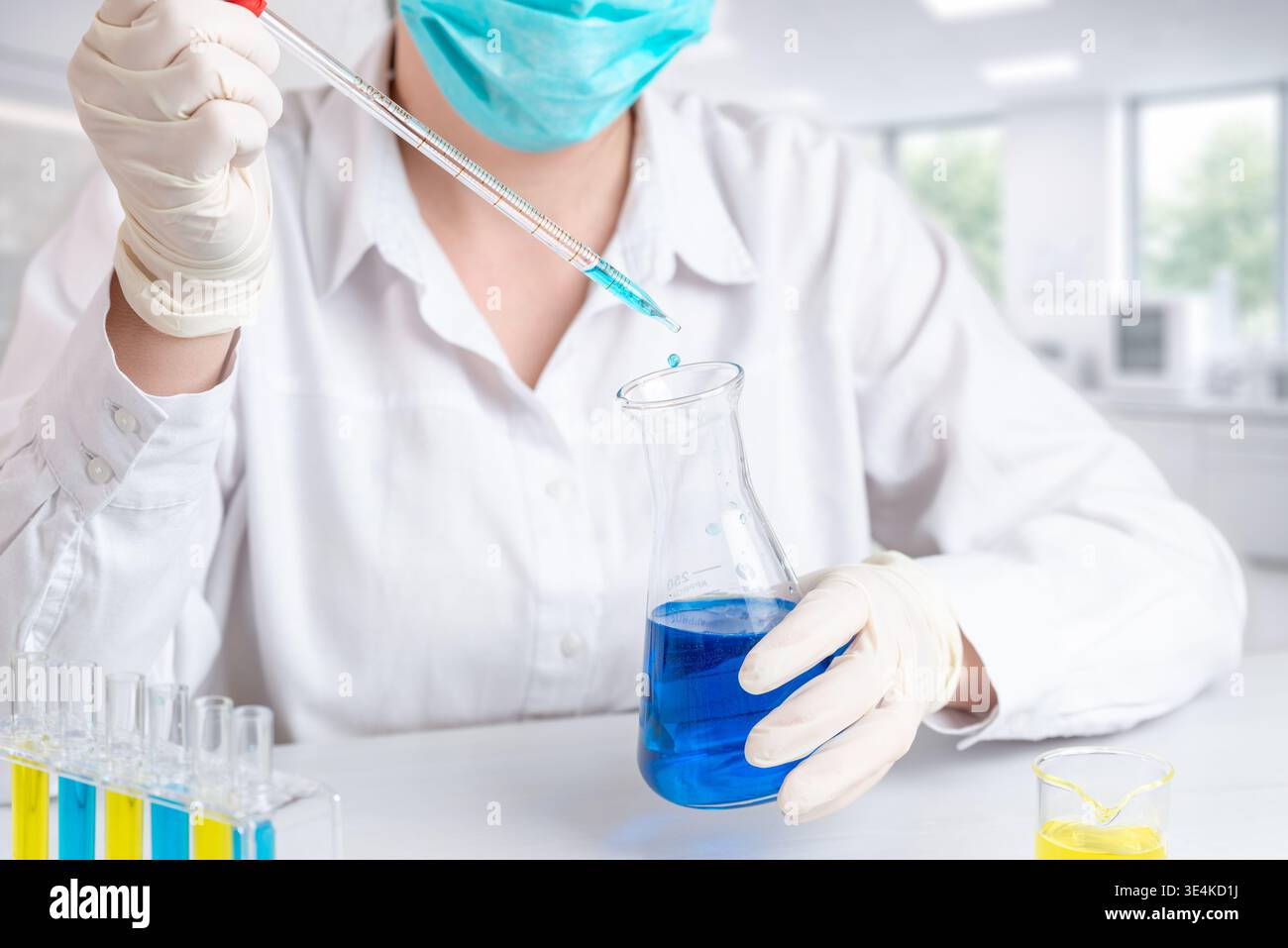 Wissenschaftler, die blaue Flüssigkeit mit Pipette, Laborversuch und chemischer Prüfung mit Präzisionstechnik in den Kolben umfüllen Stockfoto