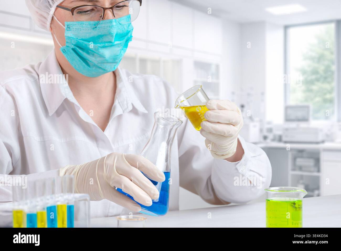 Wissenschaftler, die gelbe und blaue Flüssigkeiten in Laborglas mischen, chemische Experimente und Forschungsprozesse in kontrollierter Laborumgebung durchführen Stockfoto