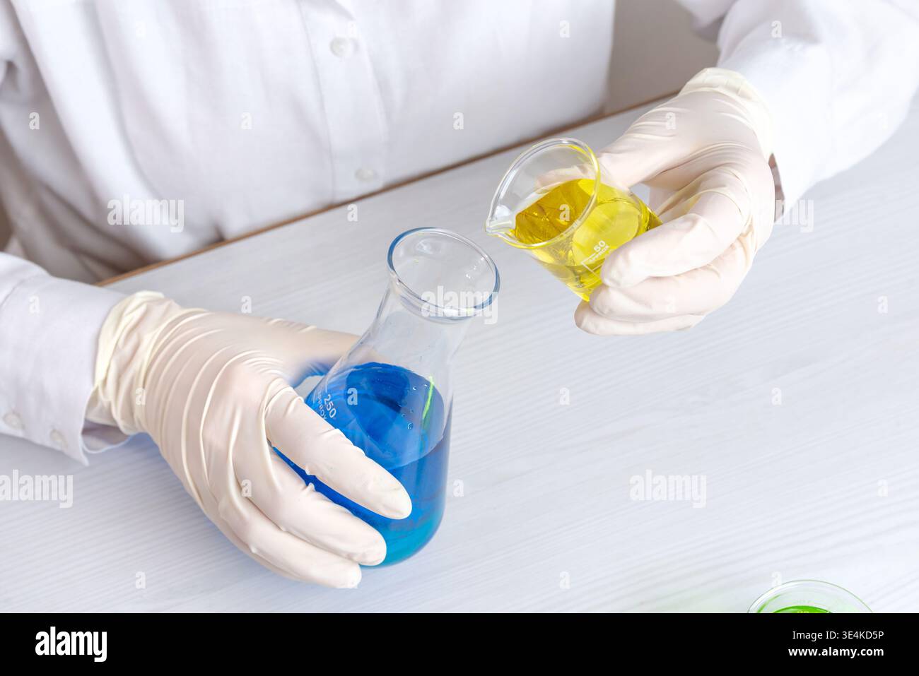 Labortechniker, der gelbe Flüssigkeit in blaue Lösung gießt, chemische Reaktion und wissenschaftliches Experiment mit kontrastierenden Flüssigkeiten Stockfoto