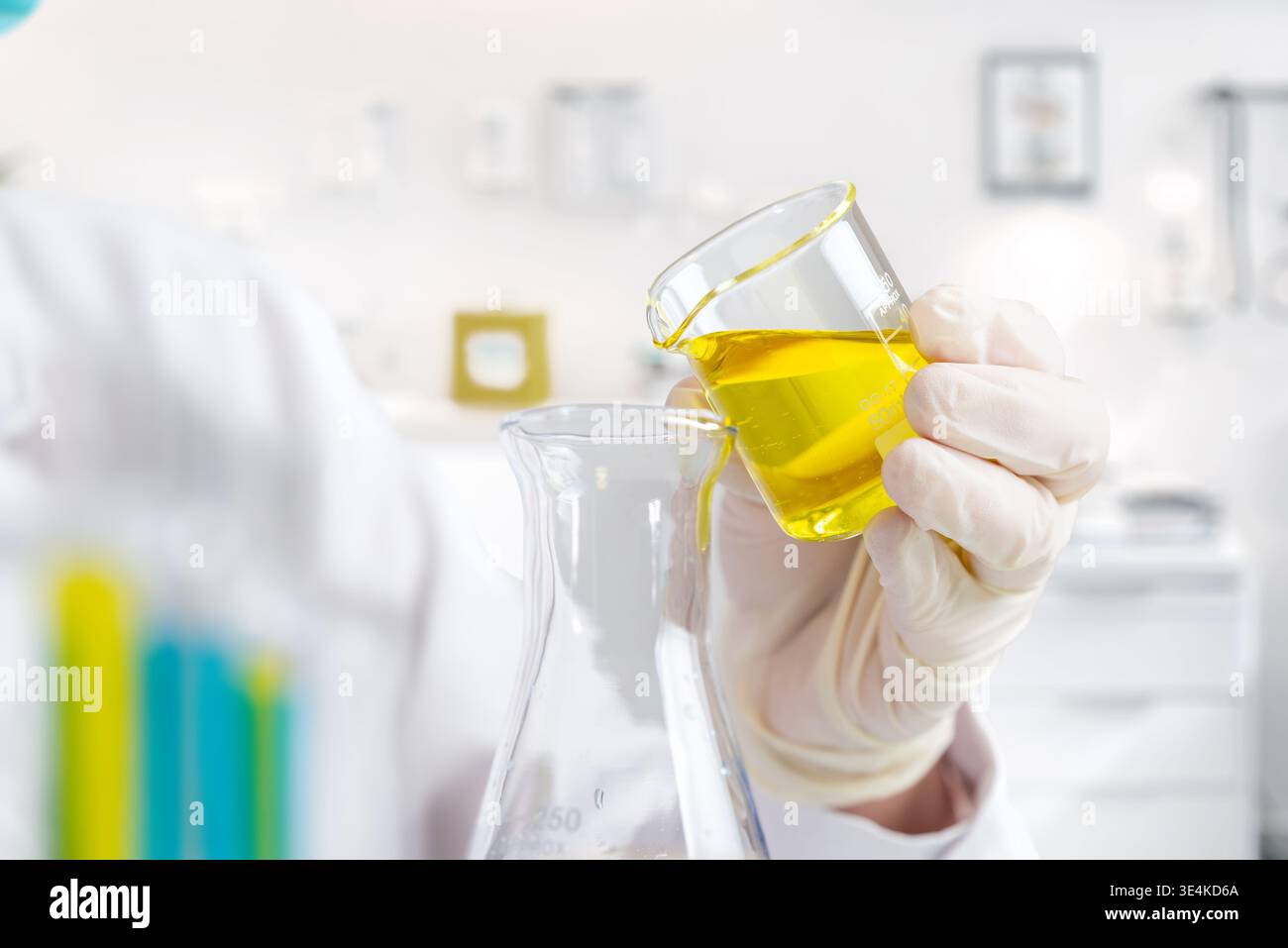 Nahaufnahme von gelber Flüssigkeit, die in Glaskolben, Laborversuch und chemisches Mischen in wissenschaftlichen Forschungseinrichtungen gegossen wird Stockfoto