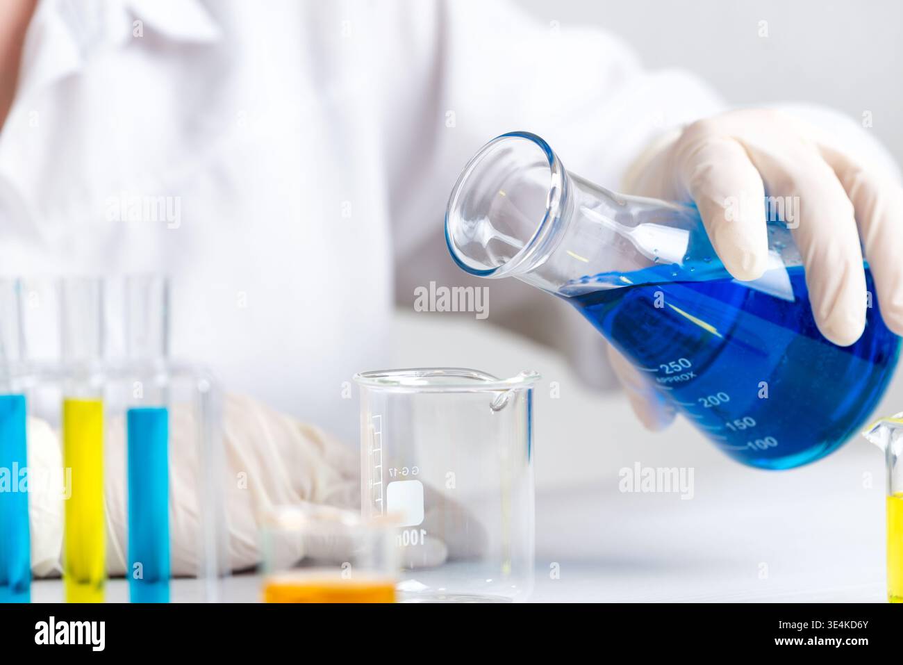 Wissenschaftler gießen blaue Flüssigkeit in leere Becher, Laborversuch und chemische Vorbereitung für die Analyse Stockfoto