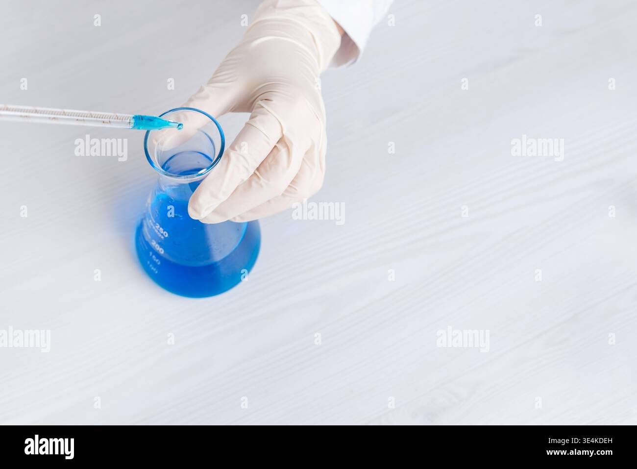 Draufsicht der Pipette, die blaue Flüssigkeit in den Laborkolben, chemische Experimente und präzise wissenschaftliche Testverfahren einfügt Stockfoto