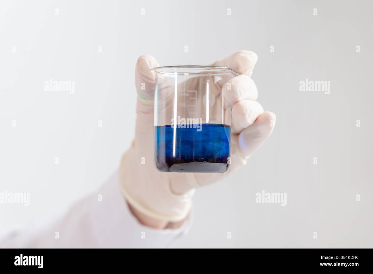 Laborbecher mit blauer chemischer Lösung und Reaktion auf dunkle Substanzen, isoliert auf weißem Hintergrund Stockfoto