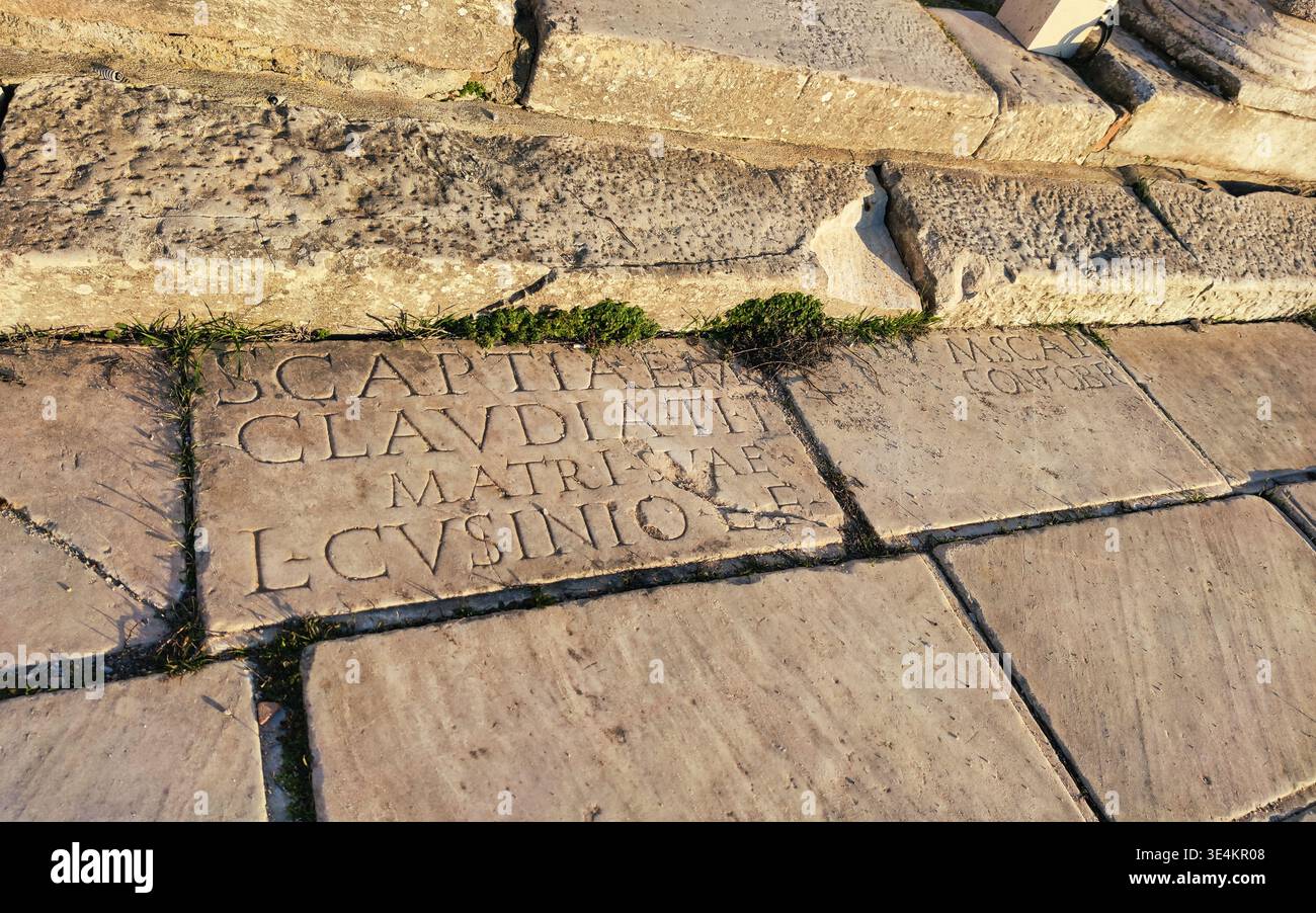 Eine hochwinklige, detailreiche Aufnahme des antiken Steinpflasters. Große Marmorplatten sind mit tief geschnitzten lateinischen Inschriften versehen, darunter Namen wie „CLAVDIAE“. T Stockfoto