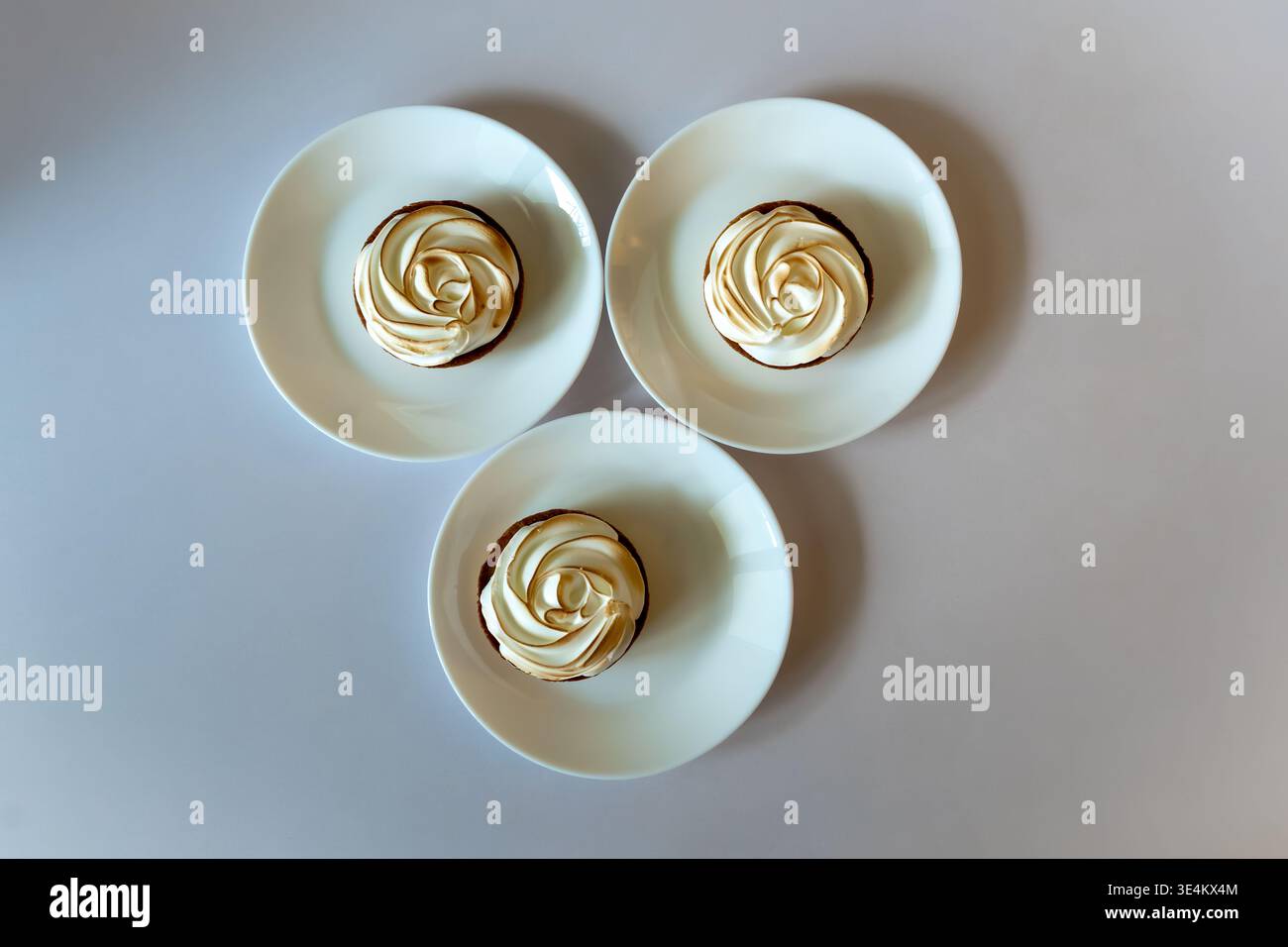 Blick von oben auf drei kleine Tartlets mit gerösteten Baisons, die jeweils auf einem weißen Teller auf hellem Hintergrund mit Kopierraum serviert werden. Stockfoto