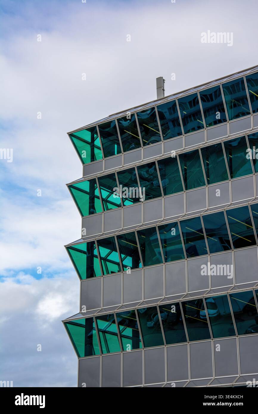 Diagonaler Blick auf eine moderne Glasfassade mit türkisfarbenen Fenstern vor bewölktem Himmel. Stockfoto