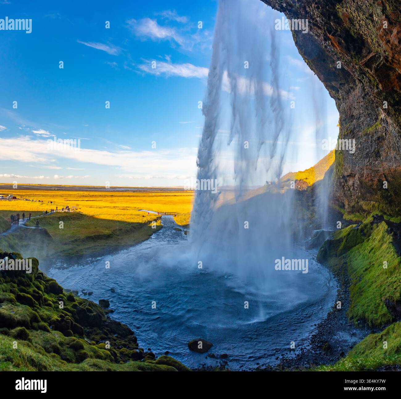 Wasserkaskaden vom Seljalandsfoss-Wasserfall und bilden einen nebeligen Vorhang. Die Szene fängt die üppige Landschaft und den atemberaubenden blauen Himmel ein und bietet ein einzigartiges Stockfoto