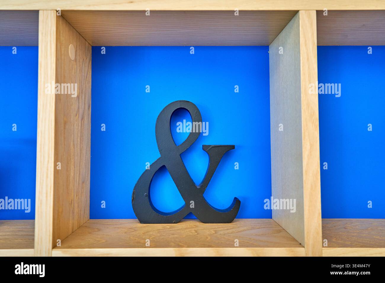Ein schwarzes dekoratives kaufmännisches und-Symbol befindet sich mitten in einem hölzernen Ablagefach vor einem leuchtend blauen Hintergrund. Das Regal besteht aus Stockfoto