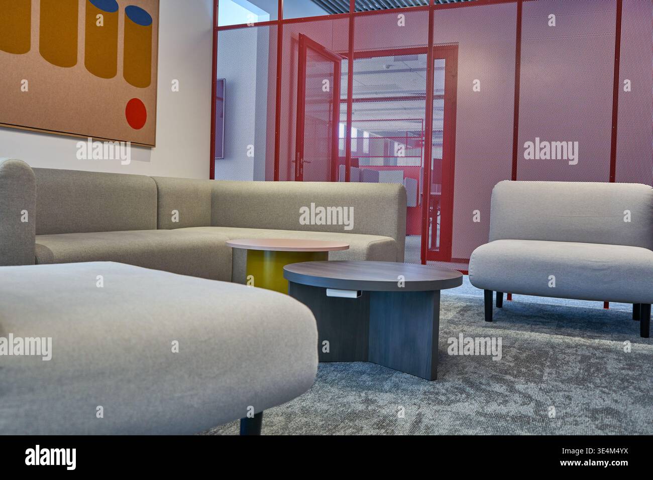 Moderner Büro-Lounge-Bereich mit grauen gepolsterten Sitzgelegenheiten und Sesseln, die um runde Couchtische mit Gelb- und Dunkelgrau angeordnet sind Stockfoto