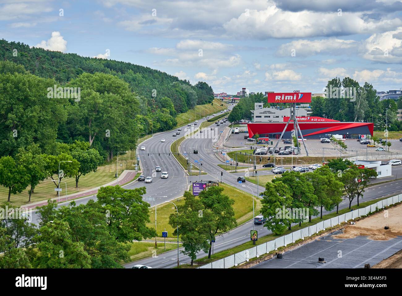 Panoramablick auf eine mehrspurige Autobahn mit moderatem Verkehr, der durch ein üppiges, grünes Stadtgebiet fließt. Auf der rechten Seite steht ein hervorstehendes Rot Stockfoto