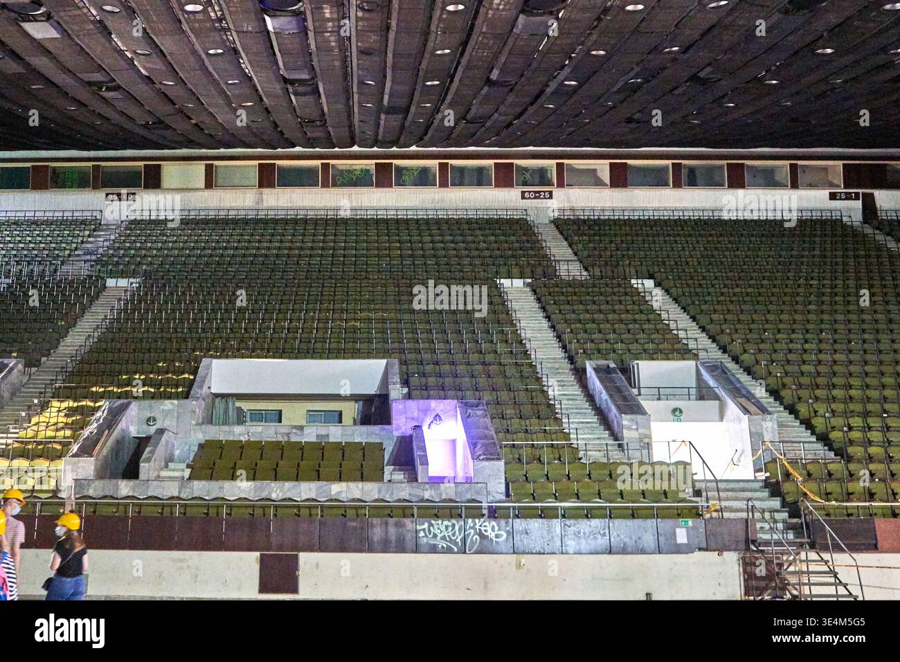 Innenansicht eines großen, leeren Stadions oder einer Arena mit Reihen grüner Sitze, die in mehrstufigen Abschnitten angeordnet sind, die durch Betontreppen getrennt sind. Die Decke Stockfoto