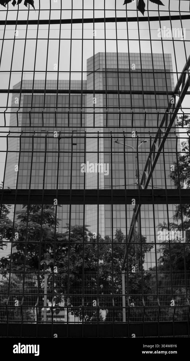 Abstrakte Ansicht der Reflexionen in einem modernen Gebäude, umgeben von einem Drahtzaun unter bewölktem Himmel Stockfoto