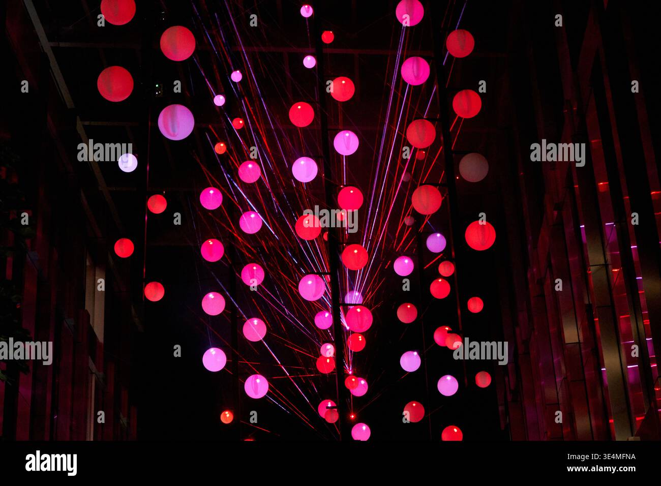 Eine lebendige Lichtinstallation für den Außenbereich mit zahlreichen beleuchteten kugelförmigen Lampen in Rot-, Rosa-, Lila- und Weißtönen, die im Dunkeln aufgehängt werden Stockfoto