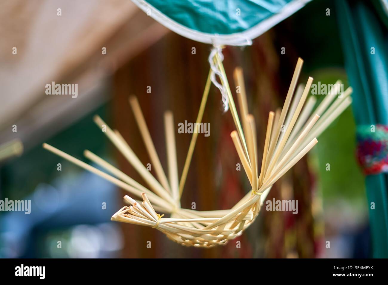 Ein Nahaufnahme eines handgefertigten, handgefertigten Strohobjekts, das einer Wiege oder einem dekorativen Korb ähnelt, an einem grünen Stoffdach vorbei aufgehängt Stockfoto