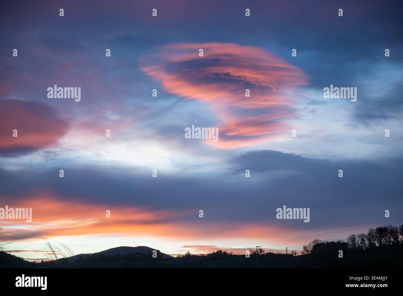 Dramatischer Sonnenuntergangshimmel mit einer einzigartigen rosa Wolkenbildung über Bergsilhouetten. Farbenfrohe Abendszene mit stimmungsvollem Licht und lebhaften Himmeltönen, Stockfoto