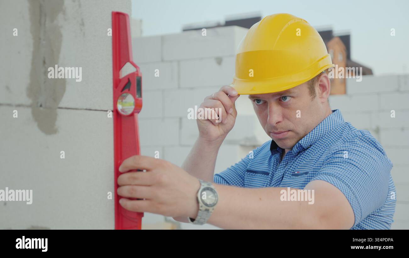 Ein Ingenieur in einem gelben Helm überprüft die Genauigkeit der Bauarbeiten. Qualitätskontrolle auf der Baustelle Stockfoto