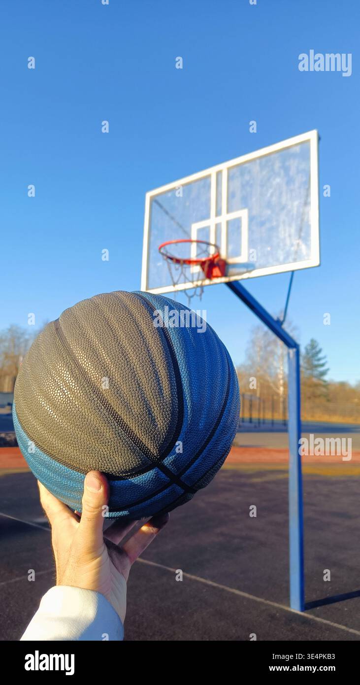 Nahaufnahme eines Basketballspielers, der den Ball hält, während er gegen den blauen Himmel steht. Erfolg, Scoring, Sieger und Zielerreichung. Stockfoto
