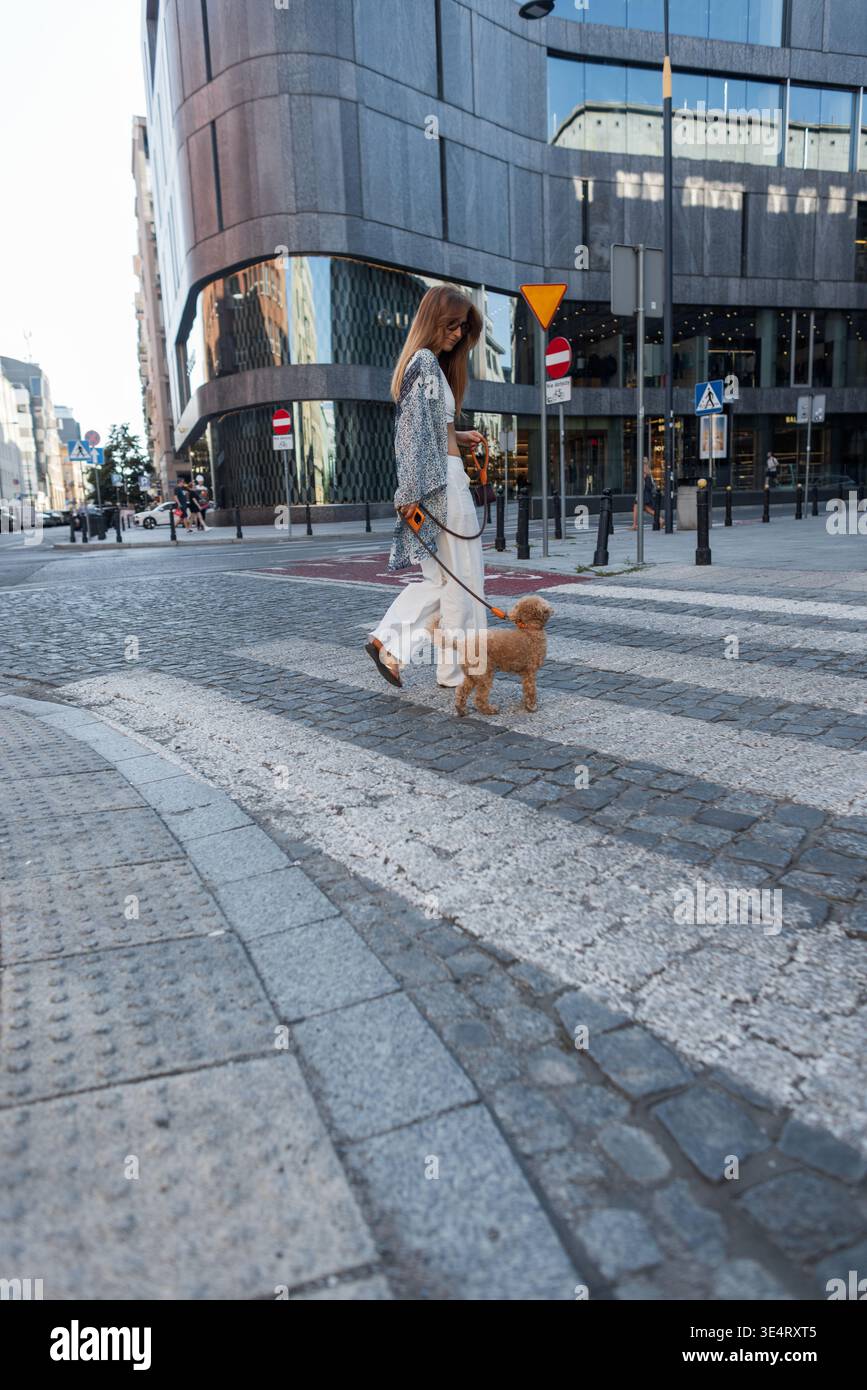Selbstbewusste junge Frau genießt einen Stadtspaziergang mit ihrem flauschigen Hund. Mode trifft Freundschaft in diesem entspannten Lifestyle-Moment Stockfoto