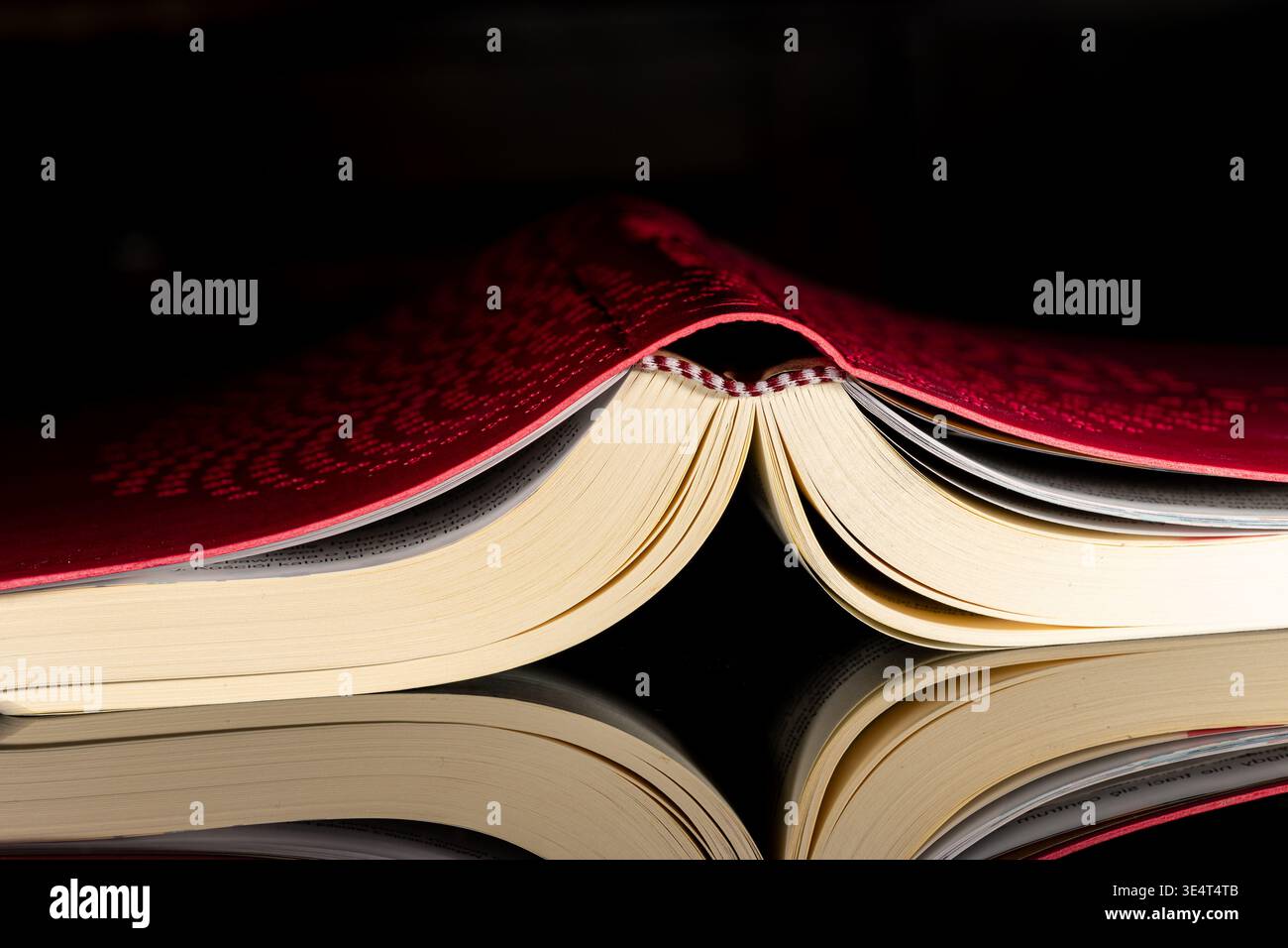 Öffnen Sie die Bibel mit rotem Cover, fotografiert auf schwarzem Hintergrund in dramatischem Licht. Religiöses Stillleben, das mit dem Christentum, dem Glauben, dem Glauben, der Scri zusammenhängt Stockfoto