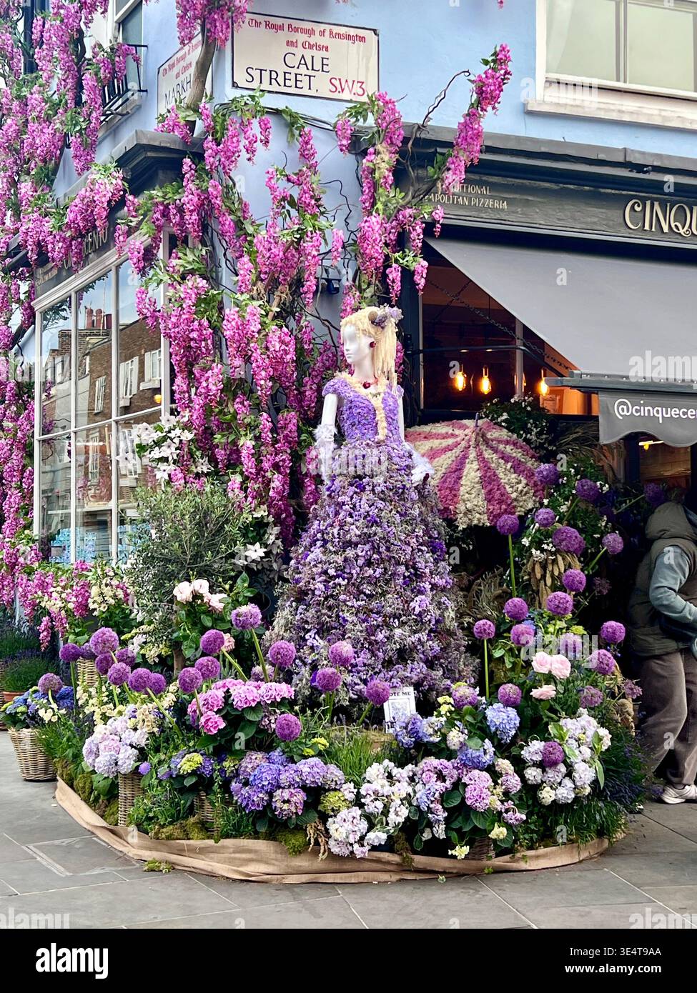 Chelsea Flower Show Display. Weibliche Mannequin mit lila Blumen, die ein Kleid bilden. Lila Allien, Glyzinien und Hortensien. Stockfoto