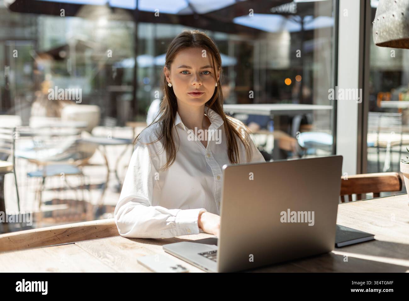 Freiberuflicher Tippdienst auf Laptop in gemütlichem Café. Moderner Arbeitsbereich mit Kaffee, Telefon und stilvollen Accessoires. Produktiver Remote-Arbeitsplatz. Frau, die arbeitet Stockfoto