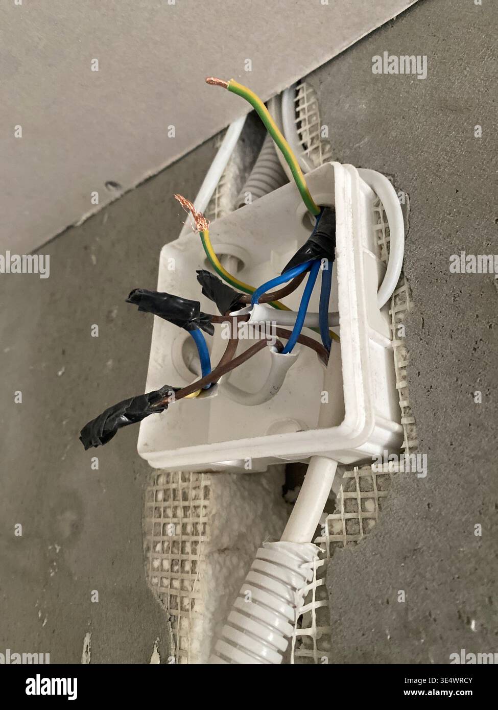 Freiliegender elektrischer Anschlusskasten, mehrfarbige Drähte, gewellter Kabelkanal, Einführungskasten, blau braun, grüngelb Stockfoto