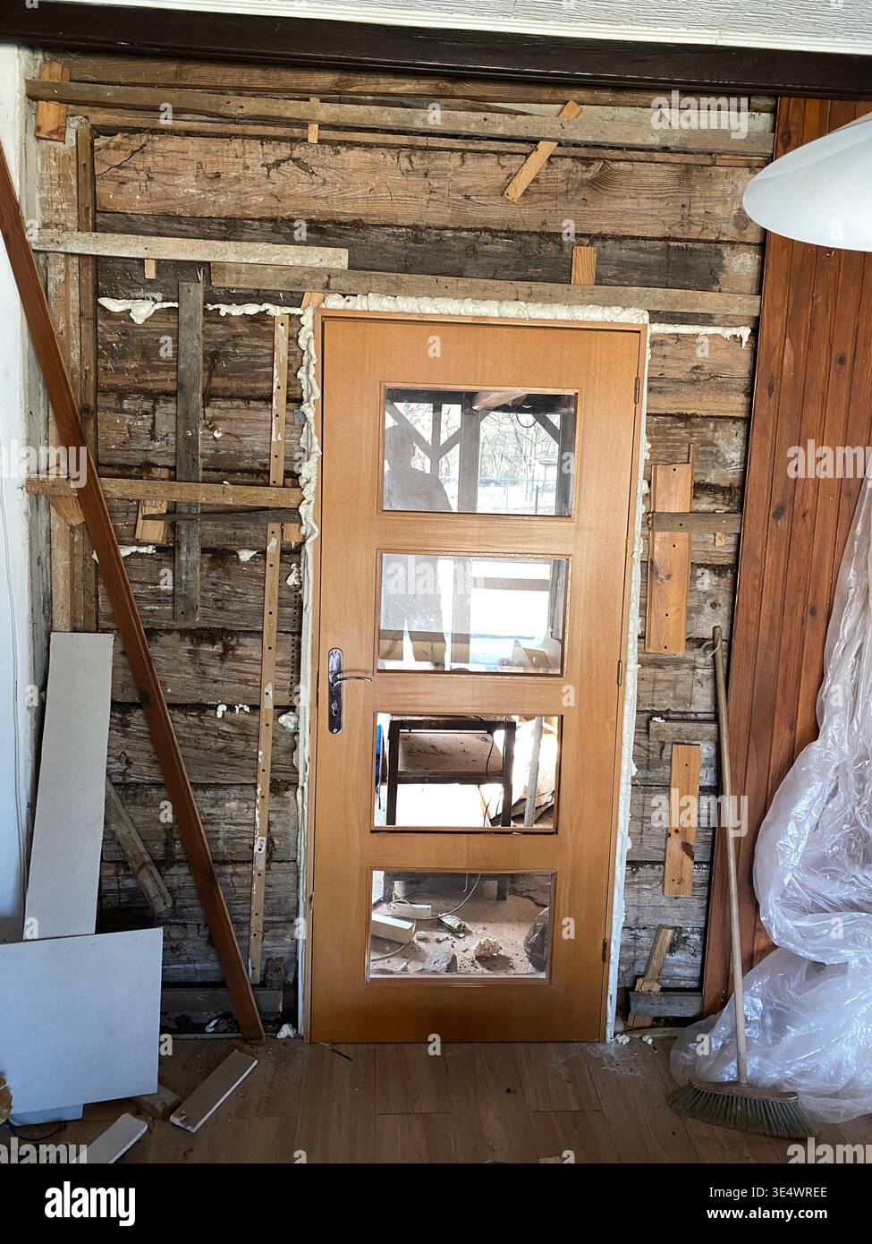 Wohnzimmerwand mit freiliegenden Nieten, alte Glasspanel-Tür intakt, verstreute Werkzeuge und Schutt auf dem Boden, Stockfoto