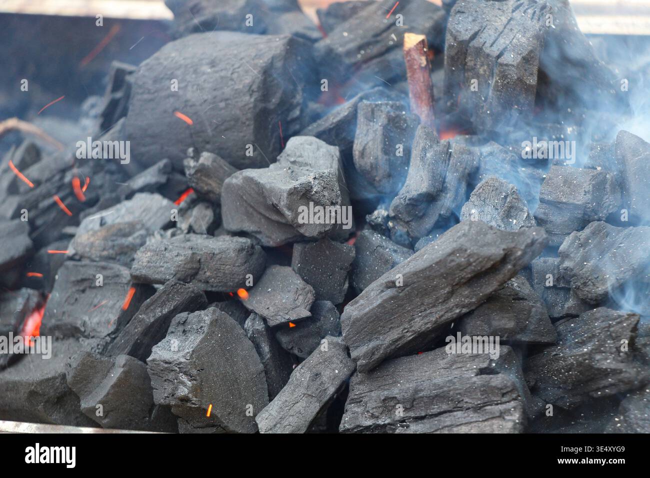 Brennende Holzkohlebriketts, die mit hellen orangen Flammen und heißer Glut glühen, erzeugen intensive Hitze für das Grillen auf Grillplätzen im Hinterhof, Campingplätzen, an Stockfoto