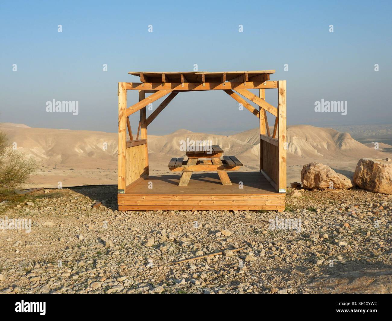 Hölzerne Picknickunterkunft mit einem Tisch, der einen Ruheplatz bietet und einen Panoramablick auf die weite trockene Landschaft des Jordan Rift Valley unter klarem Blau bietet Stockfoto