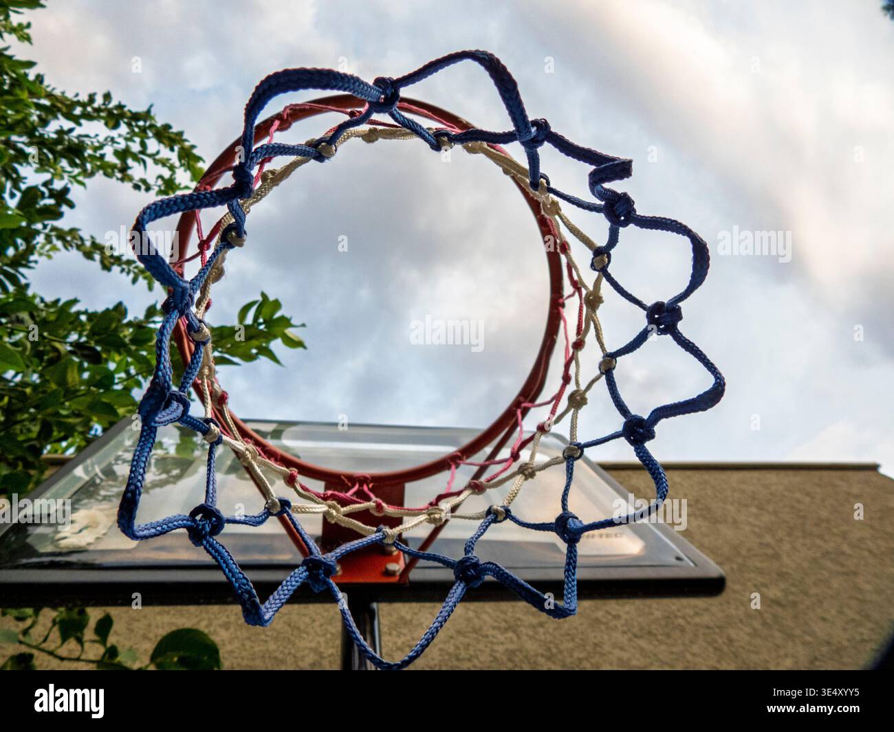 Basketballkorb aus einer einzigartigen Perspektive mit niedrigem Winkel, der das Netz und die Rückseite vor einem wolkigen blauen Himmel zeigt, was Erfolg, Erfolg und Go darstellt Stockfoto
