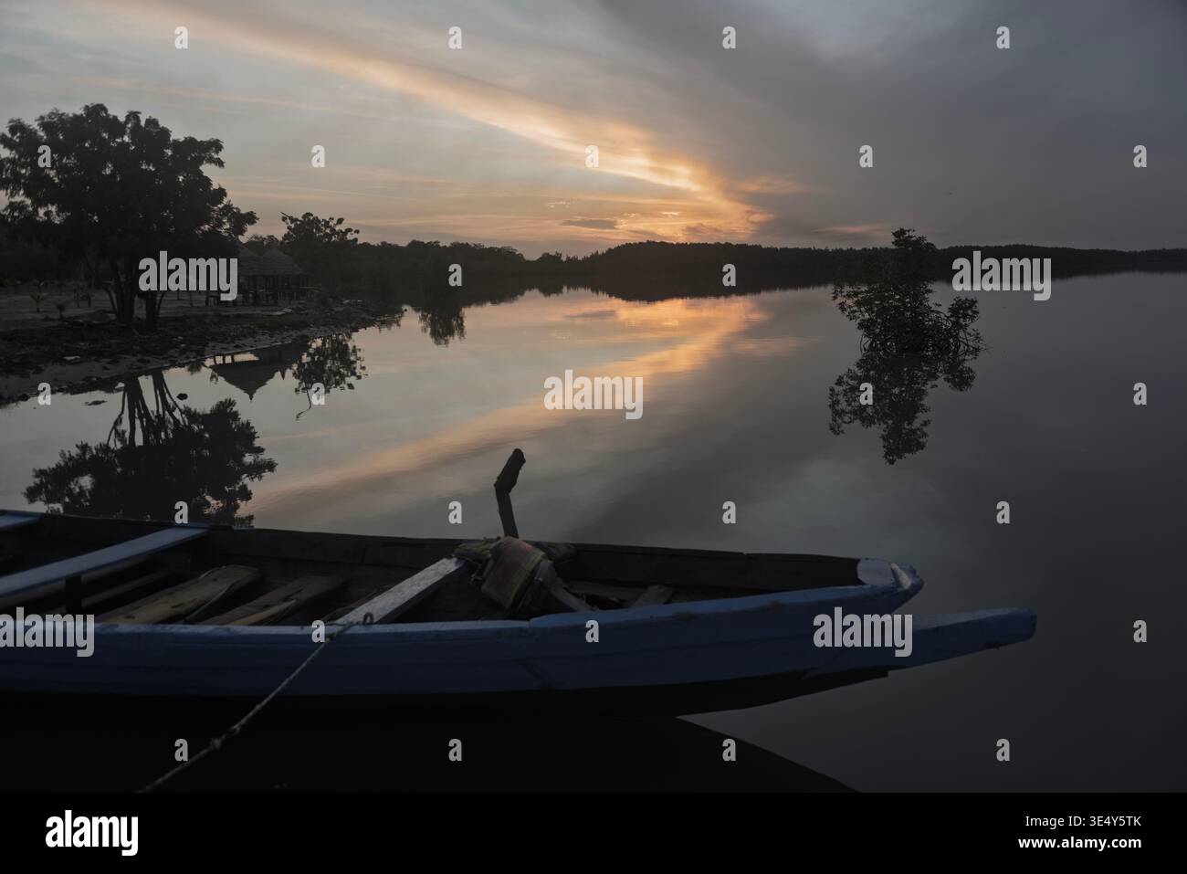 Blick auf ein blaues Holzkanu bei Sonnenuntergang an einem zerbröckelten Steg im Gambia Fluss. Tendaba, Gambia. Stockfoto