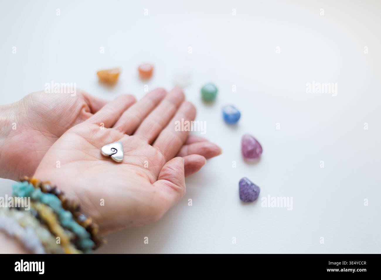 Hände, die ein Herzamulett mit einem Halbkreis aus Kristallen halten Stockfoto