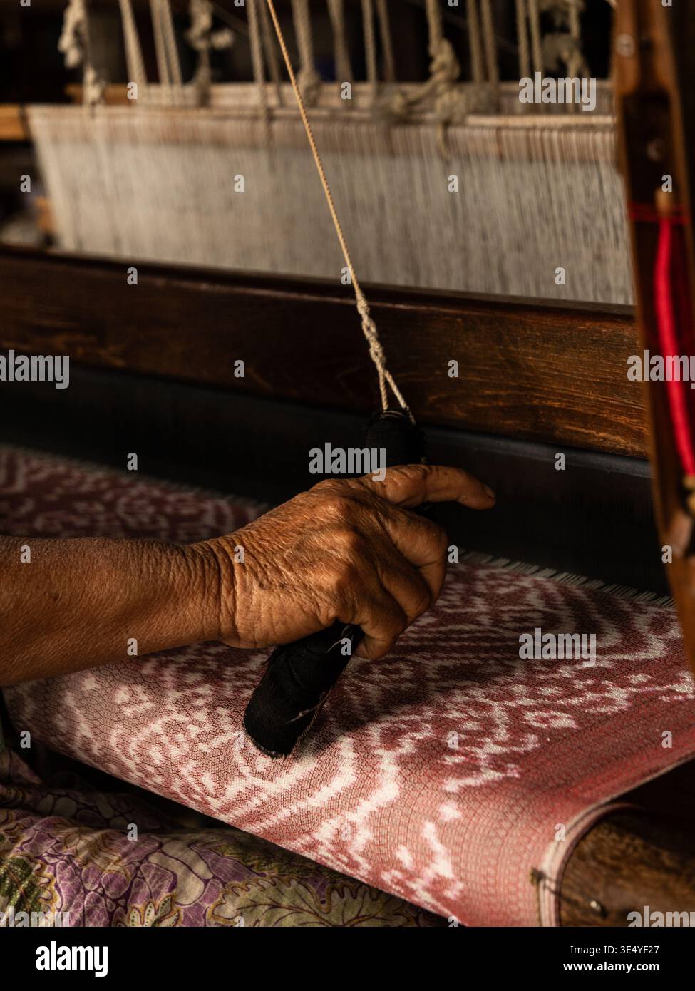 Nyaungshwe, Myanmar Birma - 26. Februar 2026: Blick auf verwitterte Hände, die das Shuttle durch den Webstuhl führen und einen Wandteppich aus komplizierten Mustern A weben Stockfoto