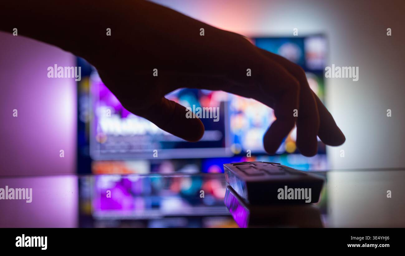 Fernseher mit Streaming mit Fernbedienung in der Nähe der Wand im Zimmer. Nachrichten und Serien online. Videos auf dem Fernseher ansehen. Die Fernbedienung des Fernsehers wird mit der Hand bedient Stockfoto