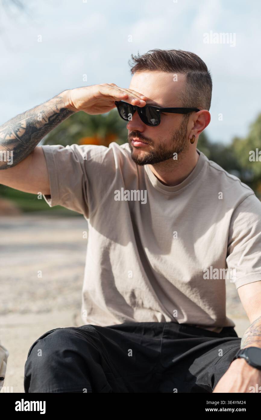 Hübscher, stilvoller Mann mit Sonnenbrille in beigem T-Shirt, der auf Stufen in Barcelona, Spanien, sitzt Stockfoto