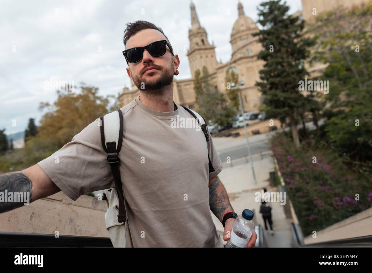 Cooler Hipster-Reisender mit trendiger Sonnenbrille in beigem T-Shirt mit Rucksack, der in Barcelona, ​​Spain, reist Stockfoto