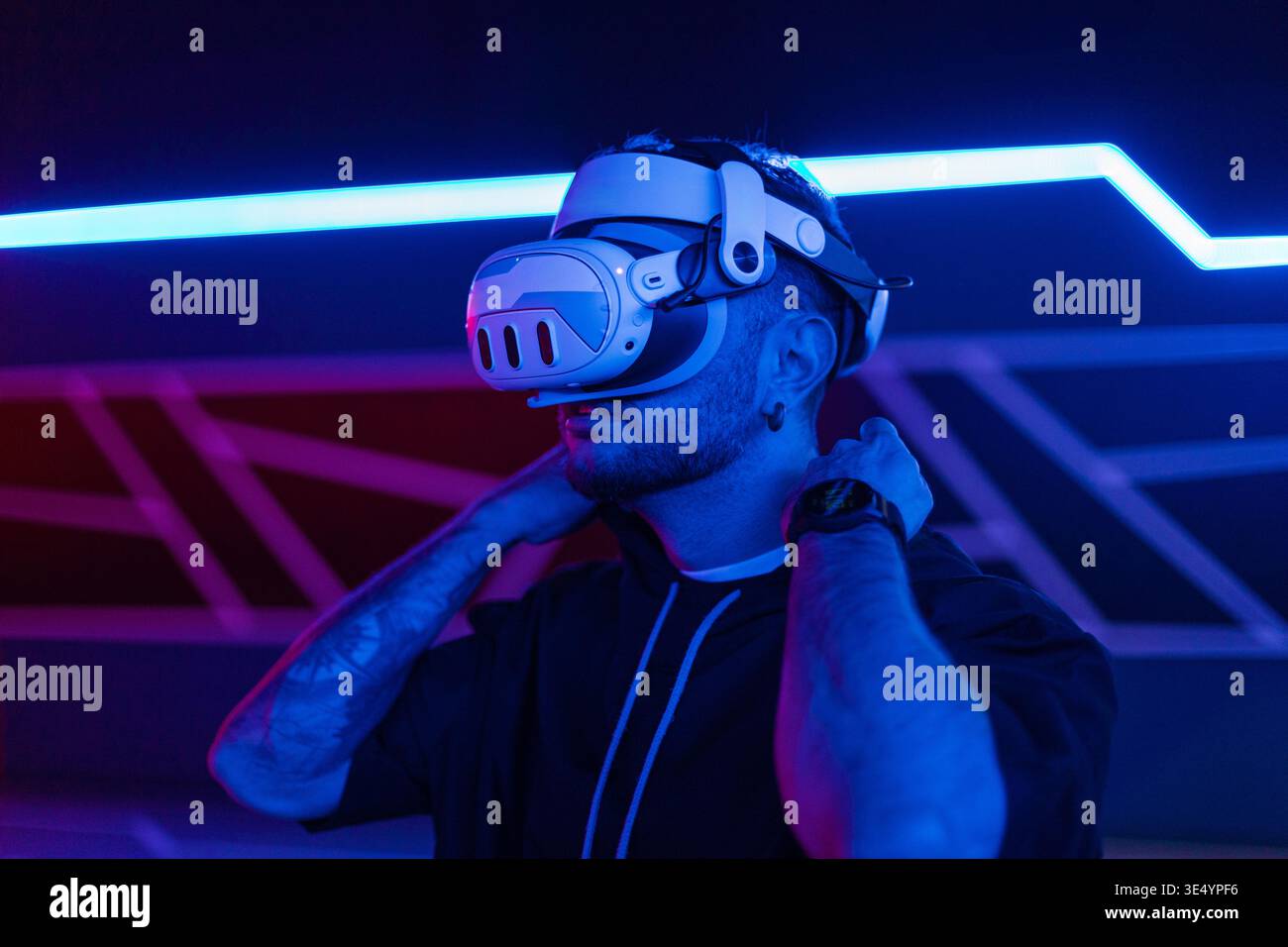 Mann in weißer VR-Brille, der Spiele in dunklem Raum mit neonrotem blauem Licht spielt. Virtuelle Realität, Konzept Stockfoto