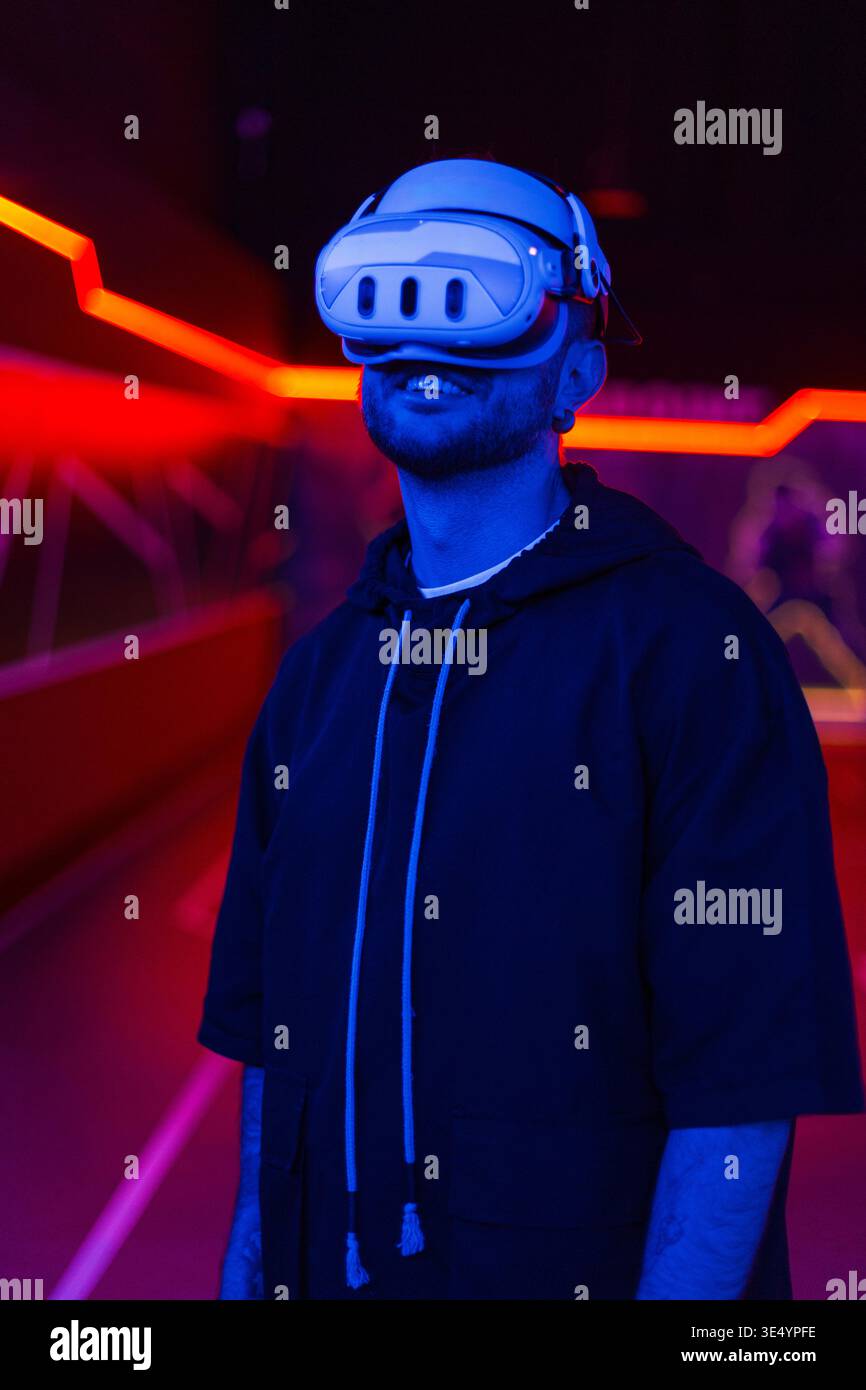 Glücklicher, gutaussehender, lächelnder Mann mit VR-Brille über virtuelle Online-Schnittstelle im Raum mit Neonlichtern Stockfoto
