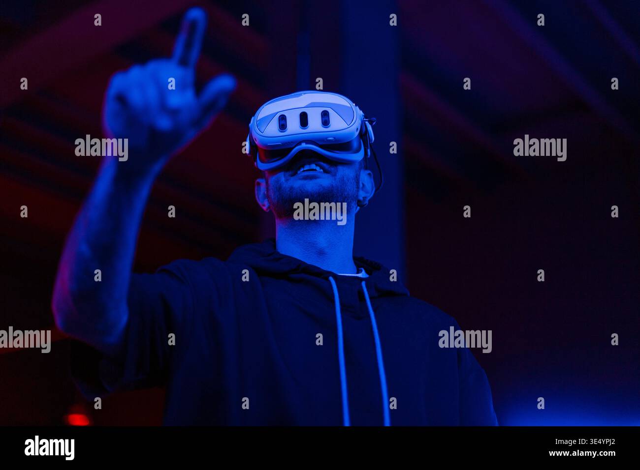 Hübscher Mann mit VR-Brille steuert die Schnittstelle mit dem Finger in dunklen Räumen mit Neonlicht. Virtuelle und erweiterte Realität. Spiele Stockfoto