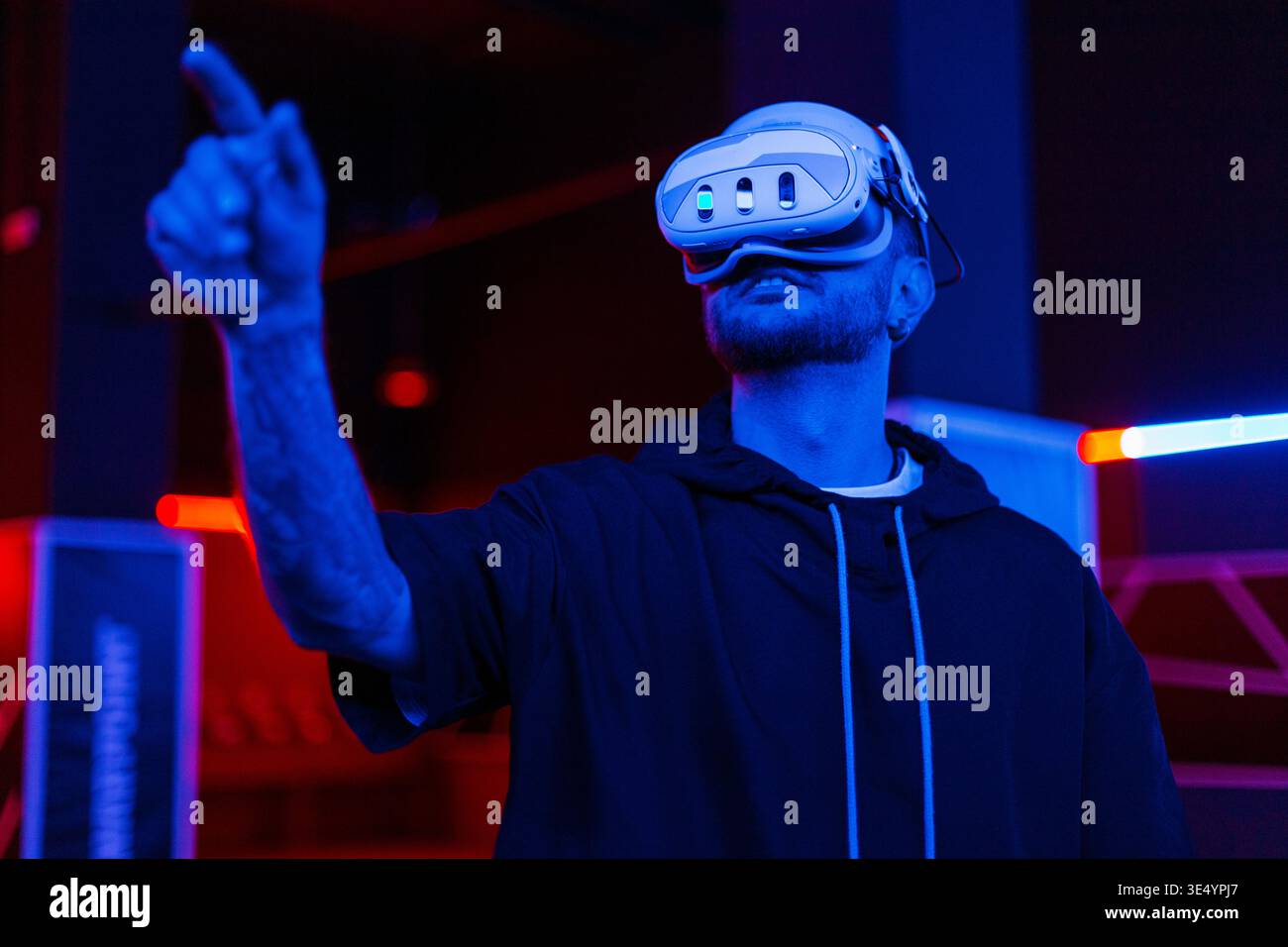 Glücklicher gutaussehender Mann in vr-Brille, der etwas spielt und versucht, etwas zu berühren, wenn er die Simulation der Welt im Dunkeln mit Neonlicht erforscht. Technologie und Stockfoto
