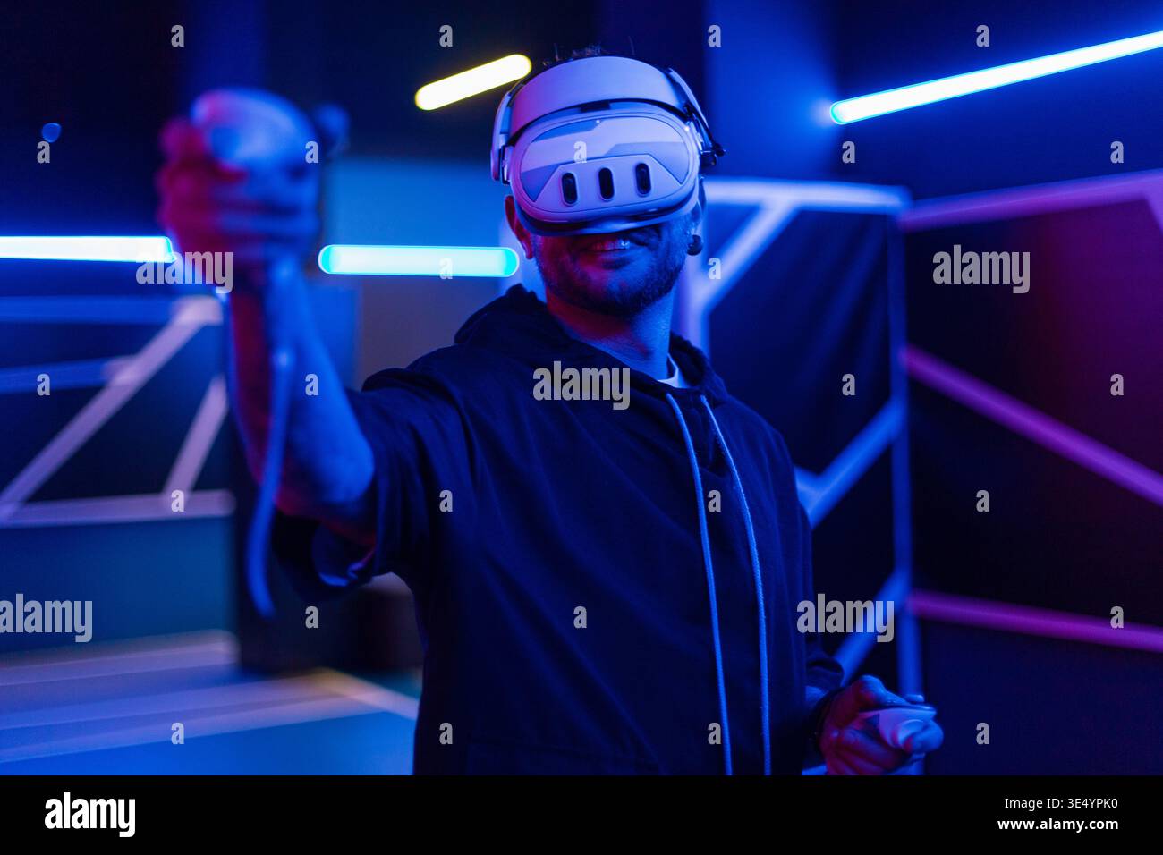 Professioneller Mann-Gamer mit VR-Brille, die Joysticks hält und virtuelles Spiel mit Neonlicht spielt. Technologie und Augmented Reality Stockfoto