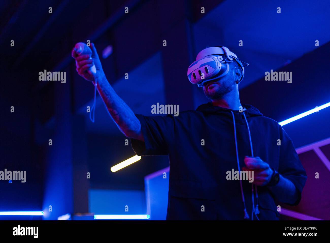 Cooler trendiger Mann in vr-Brille, der 360°-Videos mit Virtual-Reality-Headset auf dunklem Hintergrund mit Neonlicht ansieht. Der Kerl hält einen Joystick und pla Stockfoto