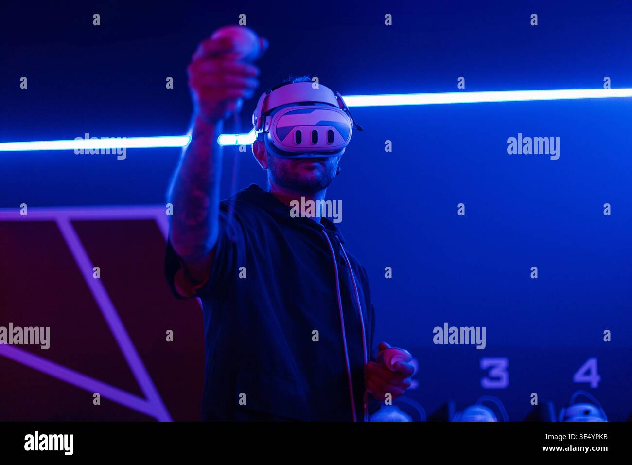 Professioneller Mann-Gamer mit VR-Brille, die Joysticks hält und virtuelles Spiel mit Neonlicht spielt. Technologie und Augmented Reality Stockfoto