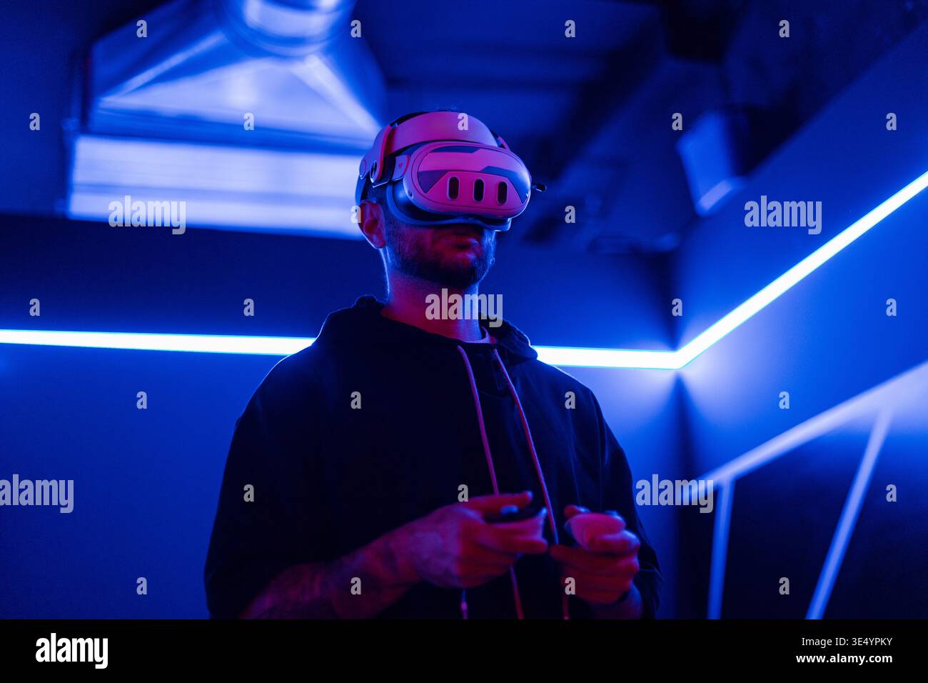 Mann mit VR-Brille, der in einem Neonzimmer spielt. Virtuelle Welt online Stockfoto