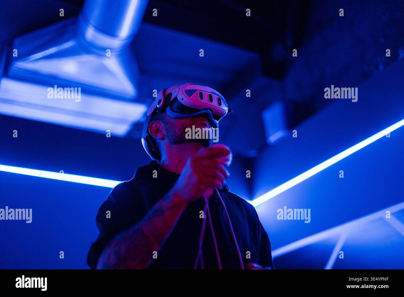 Fashion-Tech-Mann mit VR-Headset-Brille mit Joysticks, Spiel in dunklen Räumen mit Neonlicht Stockfoto