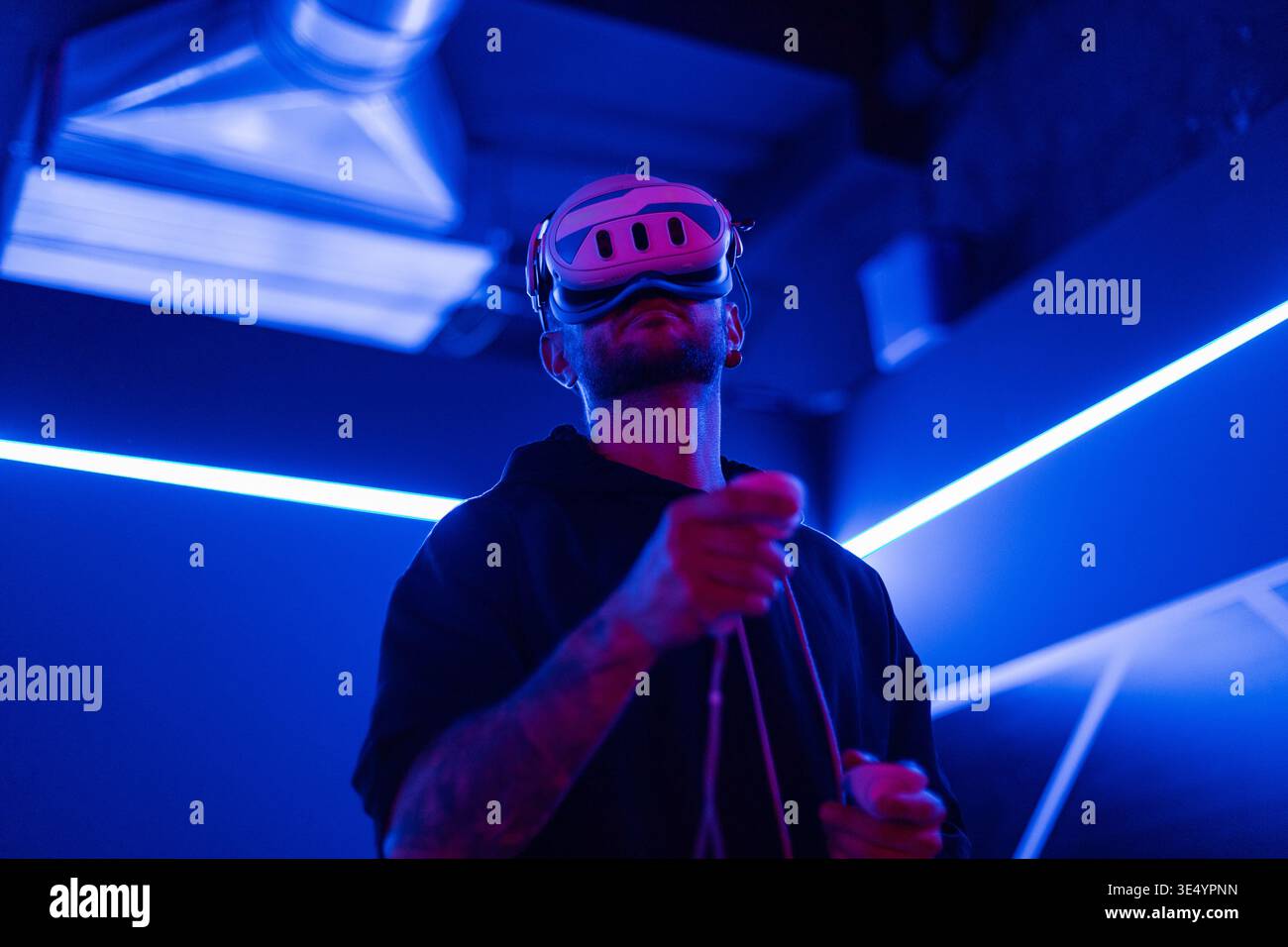 Professioneller Mann-Gamer mit VR-Brille, die Joysticks hält und virtuelles Spiel mit Neonlicht spielt. Technologie und Augmented Reality Stockfoto