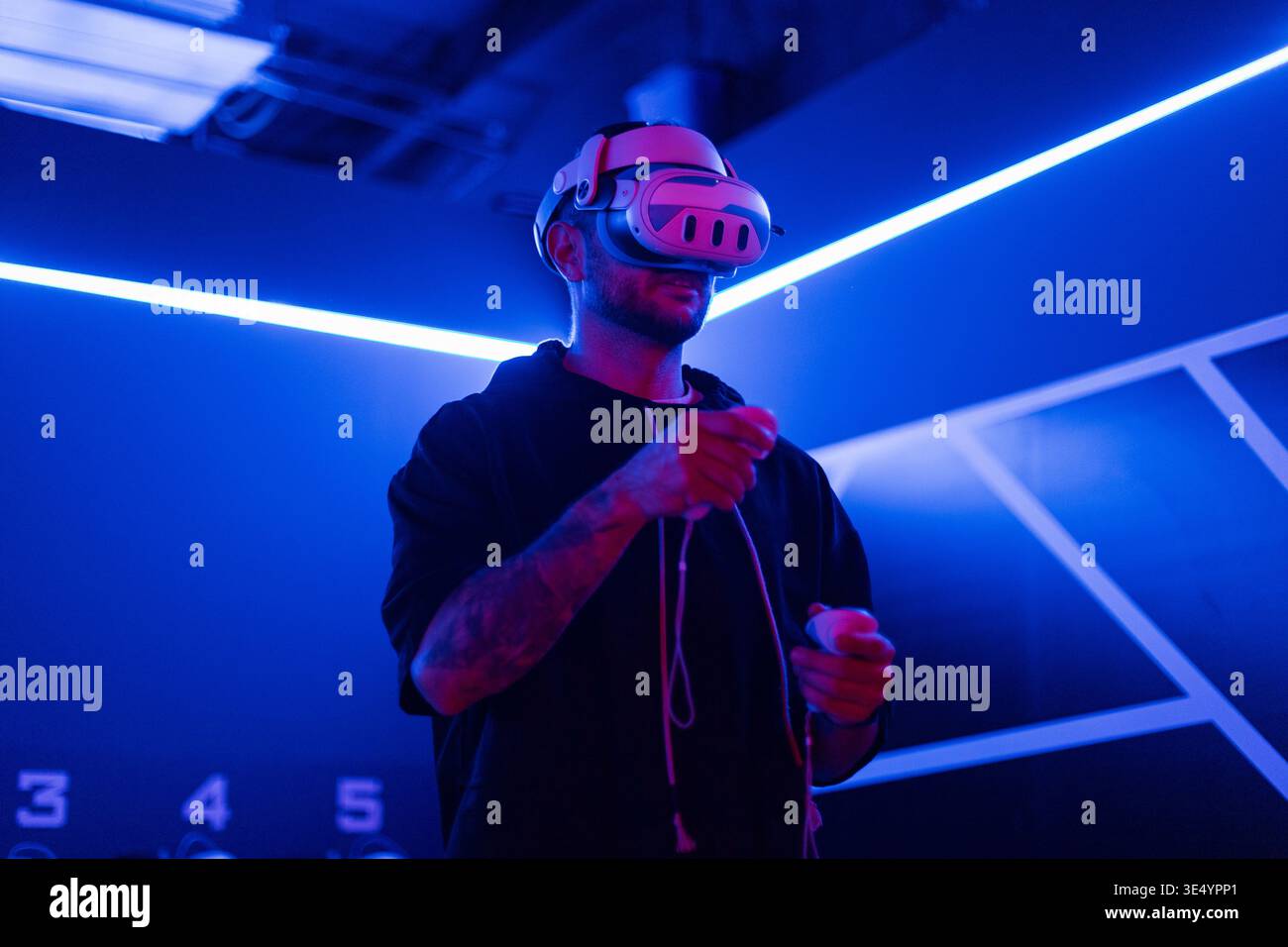 Professioneller Mann-Gamer mit VR-Brille, die Joysticks hält und virtuelles Spiel mit Neonlicht spielt. Technologie und Augmented Reality Stockfoto