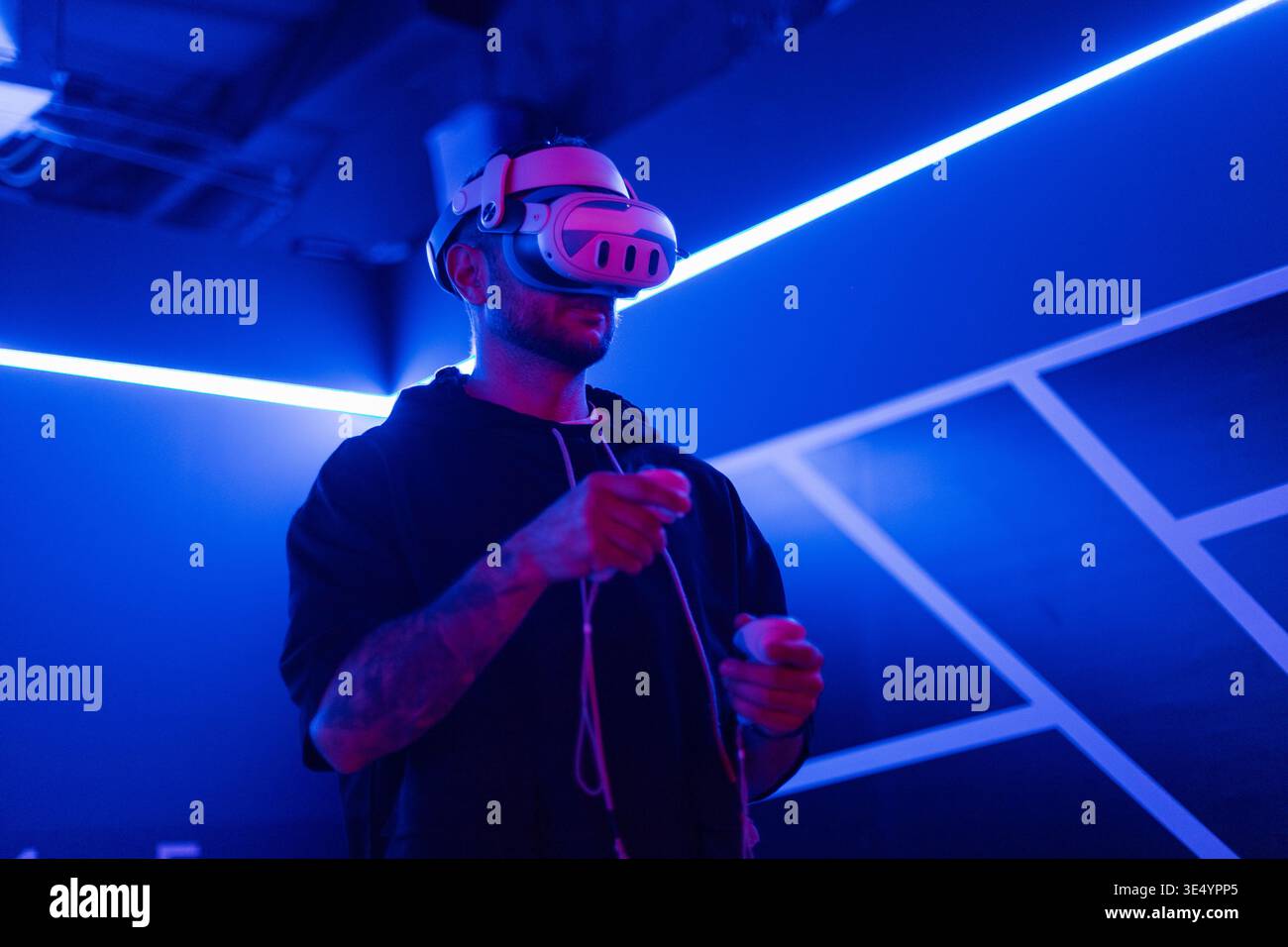 Cooler trendiger Mann in vr-Brille, der 360°-Videos mit Virtual-Reality-Headset auf dunklem Hintergrund mit Neonlicht ansieht. Der Kerl hält einen Joystick und pla Stockfoto