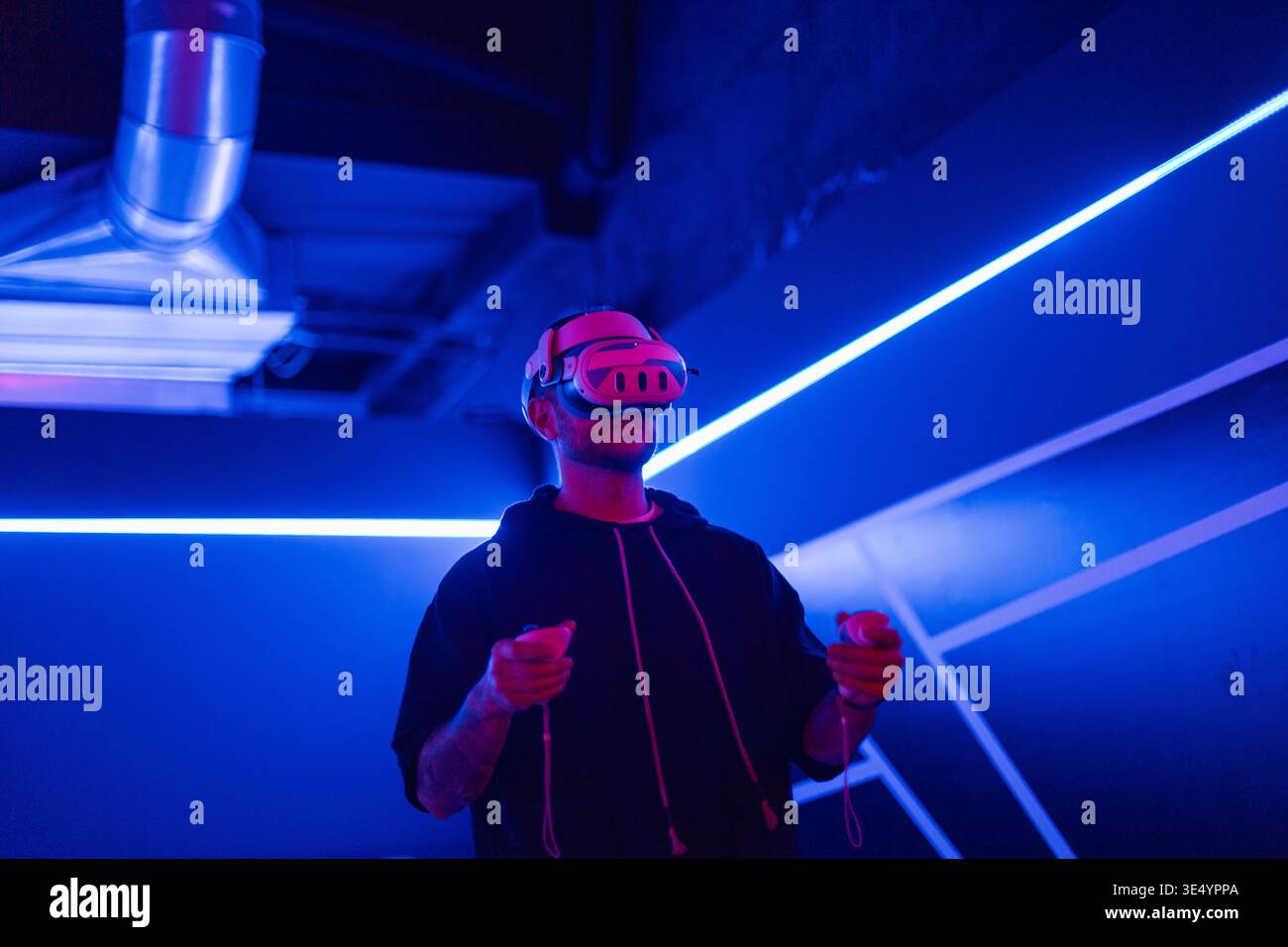 Coole Mode-Mann in VR-Headset-Brille mit Joystick, die Spiele in dunklen Räumen mit Neonlicht spielt Stockfoto
