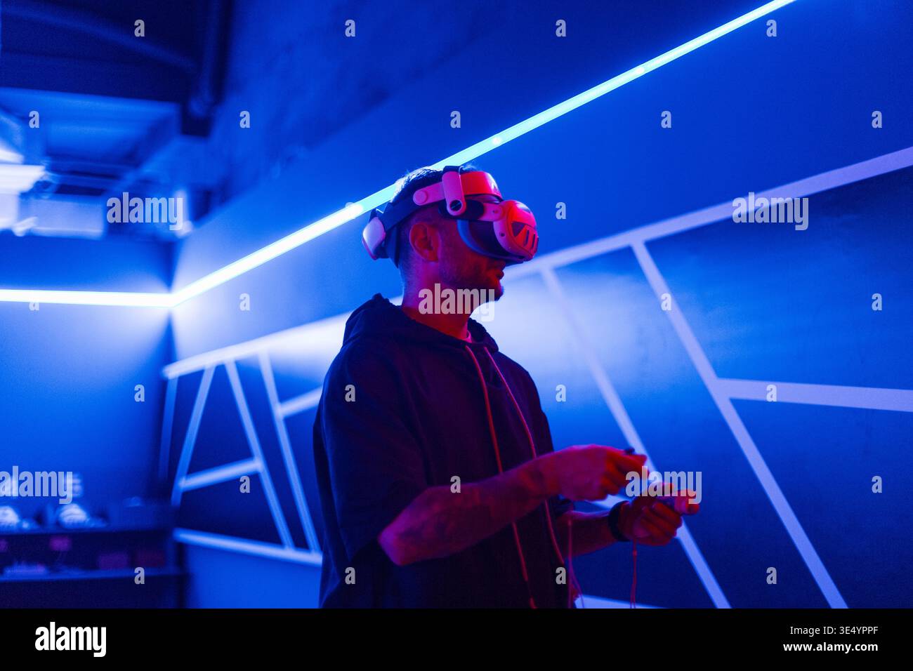 Schöner, stylischer, cooler Gamer-Mann mit VR-Brille, die Joysticks hält und virtuelles Spiel im neonhellen Spielzimmer spielt. Virtual-Reality-Technologie Stockfoto